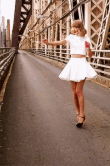 a woman in a white skirt and crop top is walking across a bridge