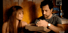 a man and a woman are looking at a box with a cw logo in the background