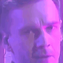 a close up of a man 's face with a blue and purple light behind him .