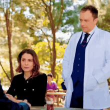 a man in a white coat and tie stands next to a woman in a black dress .