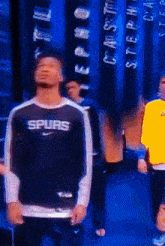 a man wearing a spurs sweatshirt stands in front of a blue wall