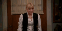 a woman wearing a white shirt and a black vest stands in front of a door