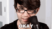 a man wearing glasses is talking into a microphone and the word okay is above him