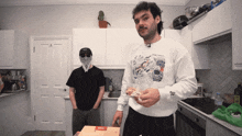 a man wearing a white sweatshirt with a skull on it holds a pizza box