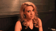 a woman with blonde hair and a black top looks at the camera
