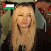 a blonde woman wearing headphones and a cat ear headband with a pixelated flag in the background