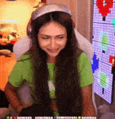 a woman wearing headphones and a green shirt is sitting in front of a computer screen .