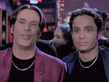 two men are standing next to each other and one is wearing a purple jacket and the other is wearing a black shirt