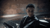a man in a leather jacket is standing next to a black car .