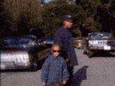 a man and two children are standing in a parking lot with cars parked behind them