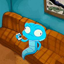 a blue cartoon character is sitting on a couch holding a remote control