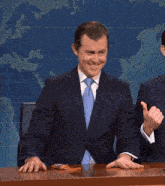 a man in a suit and tie applauds in front of a map