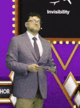 a man in a suit and tie stands in front of a blackboard with the word invisibility on it