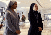 two nuns are standing in a hallway and one has a cross on her necklace