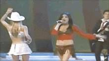 a woman in a cowboy hat sings into a microphone while another woman dances behind her