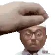 a hand is holding a man 's head with glasses and a hat .