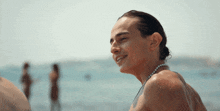 a man wearing a pearl necklace smiles at the beach