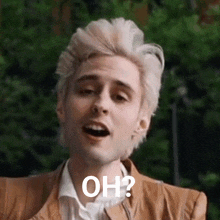 a man with blonde hair is wearing a brown jacket and a white shirt and is asking the question oh ?
