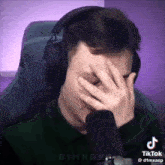 a man wearing headphones is covering his face with his hands .