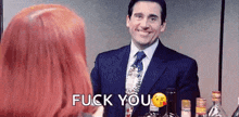 a man in a suit and tie is standing next to a woman with red hair and says `` fuck you '' .