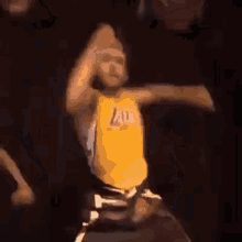 a man in a yellow lakers jersey is dancing in a dark room .