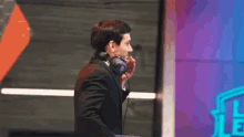a man in a suit and headphones is standing in front of a league of legends logo