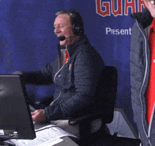 a man wearing headphones sits at a desk in front of a sign that says guar present