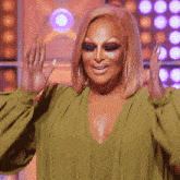 a drag queen in a green top is smiling with her hands up