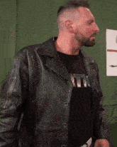 a man wearing a black leather jacket and a black t-shirt with the letter t on the front