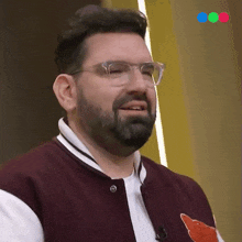 a man with glasses and a beard wearing a maroon jacket