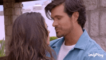 a man and a woman are kissing and the man is wearing a blue shirt and the woman is wearing a white shirt .