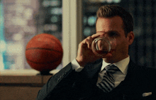 a man in a suit is drinking from a glass with a basketball in the background