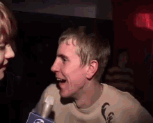 a man is talking into a microphone while another man watches .