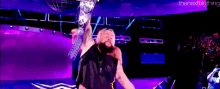 a wrestler is holding a championship belt in the air while standing on a stage .