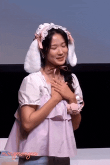 a woman wearing bunny ears holds her hands to her heart