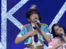 a woman in a pink dress is singing into a microphone while a man in a blue jacket sings into a microphone