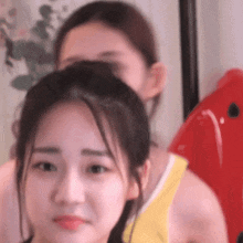 a woman in a yellow tank top is making a funny face while another woman looks on .