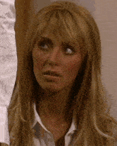 a woman with long blonde hair is wearing a white shirt and making a funny face