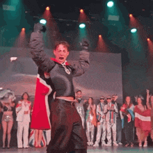 a man in a black jacket is dancing on a stage with a group of people