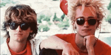 two young men wearing sunglasses are sitting next to each other and looking at the camera .
