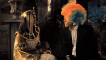 a man in a suit and a woman in a clown wig are sitting next to each other