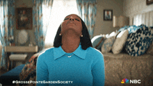 a woman in a blue sweater is sitting in a bedroom with the nbc logo on the bottom