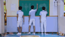 three boys are standing in front of a chalkboard and writing on it