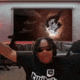 a man wearing headphones and sunglasses is standing in front of a screen with a picture of a cat on it .