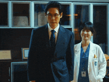 a man in a suit and tie is standing next to a woman in a white lab coat