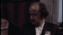 a bald man in a suit and tie is making a funny face while holding his hands up .
