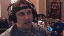a man wearing headphones is sitting in front of a microphone in a living room with a picture on the wall that says kink