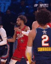 a basketball player wearing a red all star jersey talks to another player wearing a blue jersey with the number 2 on it