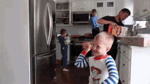 a boy in a striped shirt is standing in a kitchen while a man holds a box of kraft dinner