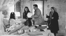 a black and white photo of a group of people standing around a baby in a hospital bed .